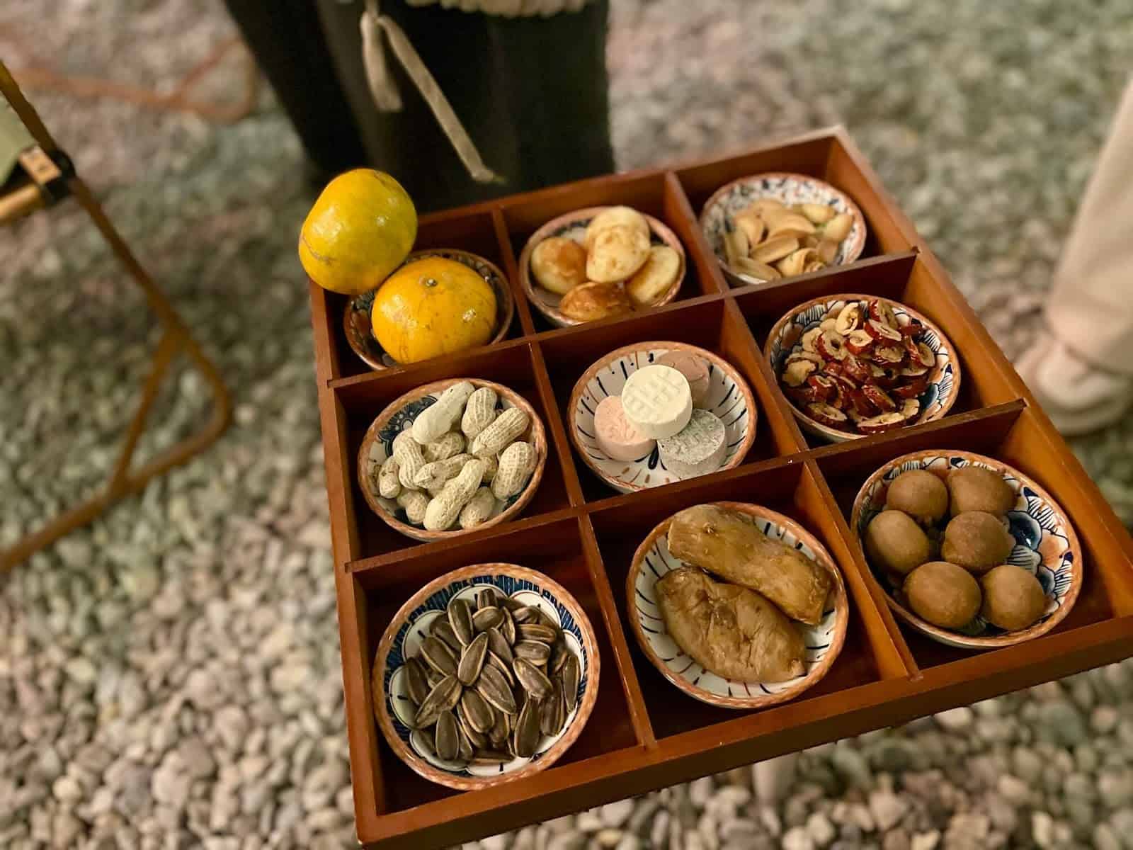 團爐煮茶的茶點，用九宮格裝著，有橘子、龍眼、地瓜、切片紅棗、帶殼花生與瓜子、糕點與小鬆餅及餅乾